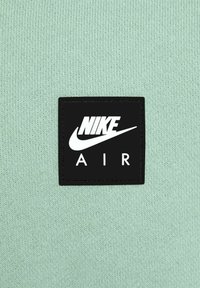 Mintgrön stickad tyg har en svart fyrkantig etikett med vit text "NIKE" ovanför "AIR" och en vit Nike swoosh-logotyp.