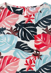 Gros plan sur un tissu à motif floral avec de grandes feuilles tropicales rouges, roses, bleu clair, noires et marron sur un fond clair, avec une petite fermeture éclair au dos.