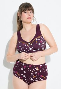 Lila gepunktetes Dessous-Set. Besteht aus einem gepolsterten BH mit breiten Trägern, einer akzentuierten Schleife und hochgeschnittenen Panties mit einem gepunkteten Muster in mehreren Farben.