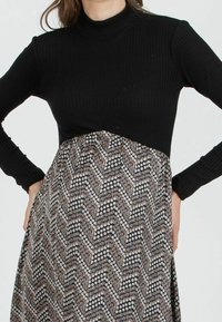 Haut noir à manches longues côtelé associé à une jupe à motifs comprenant des motifs circulaires et un design en zigzags dans des tons terreux.