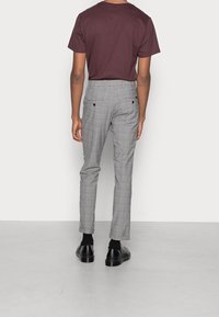 Šedé kostkované kalhoty se slim fit, spárované s vínovým tričkem. Boty jsou černé, s hladkým povrchem.