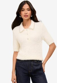 Suéter de polo blanco esponjoso con mangas cortas, botones de perla y un acabado suavemente texturizado. Presenta un cuello con un borde decorativo.