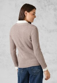 Gerippter Strickpullover in hellem Beige, mit einem weißen Kragenhemd darunter, langen Ärmeln und einer lockeren Passform, strukturierter Oberfläche und Rückennaht-Detail.