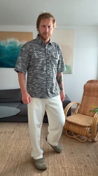 Camisa de manga curta, com botões, apresentando um padrão de ondas em preto e branco, combinada com calças brancas e tamancos cinzas. Design simples e casual.