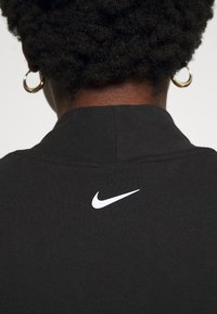 Čierna polo tričko Nike s bielym logom swoosh na chrbte, s textúrovanou tkaninou a klasickým dizajnom goliera.