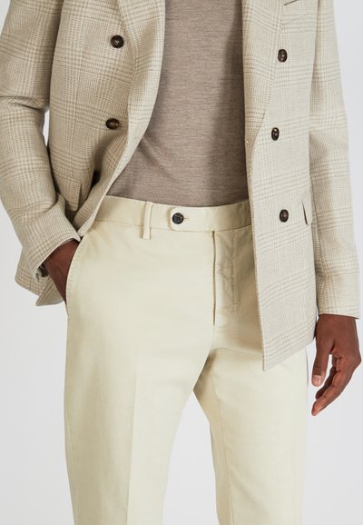 Helle, strukturierte Blazer mit einem Karomuster, kombiniert mit beigen Hosen mit Knopfverschluss und Seitentaschen.