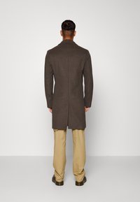 Cappotto di lana marrone con una vestibilità su misura, maniche lunghe e schiena foderata. Abbinato a pantaloni beige e scarpe scure. Design semplice e funzionale.
