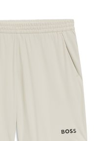 Bézs színű sportnadrág elasztikus derékpánttal, oldalzsebekkel és egy fekete "BOSS" logóval az alsó lábszáron. Simális, könnyű anyagból.