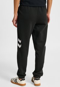 Sorte joggers med elastisk talje og manchetter, der har hvide chevronstriber på ydersiden af låret. Fremstillet af blødt, strækbart materiale.