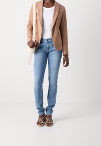 Beige kavaj, vit topp, ljusblå jeans och remsandaler. Kavajen har en enkel knapp; jeansen är åtsittande med lätt blekning.