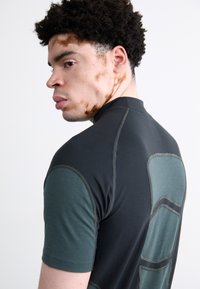 Camisa de mangas curtas preta e verde com uma textura suave. Apresenta um grande painel verde claro nas costas e detalhes de costura contrastantes.