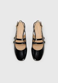 Juodos lakinės odos slingback bateliai su dviem horizontaliomis juostelėmis, dekoruotomis auksinėmis apvaliomis detalėmis. Suapvalintas pirštas ir paminkštintas dramblio kaulo spalvos padas.