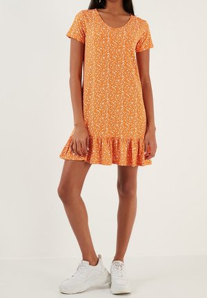 Vestido naranja con estampado floral blanco, mangas cortas y dobladillo con volantes. Se lleva con zapatillas blancas, hecho de tela suave y ligera.