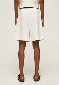 White linen shorts with a loose fit, featuring a waistband with belt loops and two back pockets. Hem finishes are clean and simple.