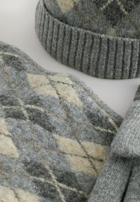 Šedá pletená čepice a šála s argyle vzorem v jemně šedých a béžových tónech. Materiály vypadají měkce a strukturovaně, s žebrovanými okraji.