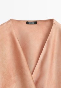 Hellbraunes V-Ausschnitt-Kleidungsstück mit glatter Stoffstruktur und einem schwarzen Etikett mit der Aufschrift "Massimo Dutti, Made in Portugal" im Nackenbereich.