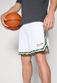 Baltie basketbola šorti ar elpojošu sietu tekstūru, ar krāsainu abstraktu rakstu uz apakšējās malas un melnu Nike logo.
