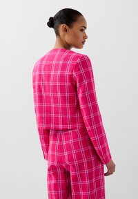 Chaqueta de cuadros fucsia con mangas largas y diseño corto, que presenta un patrón a rayas blanco y un detalle de botones en los puños.