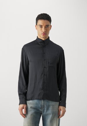 Zwarte blouse met knoopsluiting, gemaakt van een gladde stof; heeft een hoge kraag, lange mouwen, een voorzak en een relaxte pasvorm.