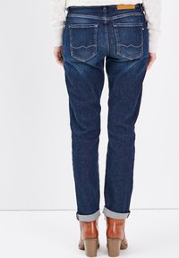 Jean en denim bleu foncé avec une coupe droite, des poignets retroussés et deux poches arrière avec des coutures courbes.