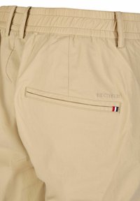 Shorts beige clair en matériau léger. Dotés d'une taille élastique, d'une poche arrière avec zip et d'un détail logo avec des accents rouge, blanc et bleu.