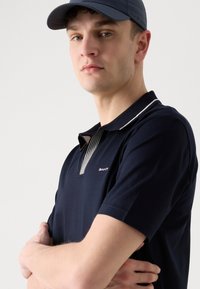 Camisa polo azul marino con un cuello a rayas, mangas cortas y un pequeño logo en el pecho. Textura de algodón suave, corte relajado.