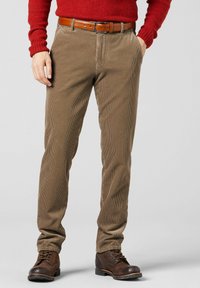 Bruine corduroy broek met verticale strepen, voorzakken en een bruine leren riem; gecombineerd met donkerbruine veterlaarzen en een rode trui.