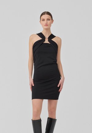 Black sleeveless dress with twisted neckline and circular accent. Form-fitting design and smooth texture, paired with knee-high black boots.
