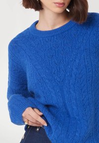 Maglione lavorato a maglia di un blu brillante con motivo geometrico, scollatura rotonda e maniche oversize. Consistenza morbida con polsini a coste.