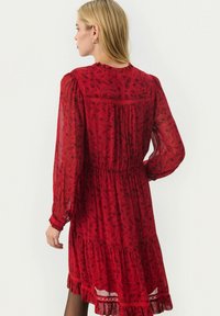 Rode bloemenjurk met lange mouwen, een gathered taille en gelaagde ruffles aan de zoom. Gemaakt van doorschijnende stof met ingewikkelde patroondetails.