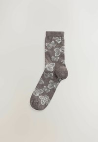 Chaussette grise avec des motifs papillons blancs, posée à plat sur un fond neutre clair.