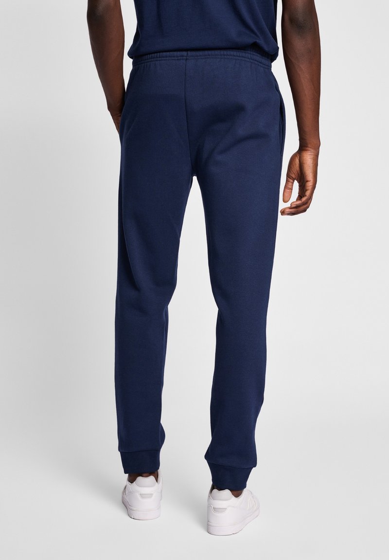 Navyblaue Jogginghosen aus weichem Stoff, mit einem elastischen Bund, schmal zulaufenden Beinen und gerippten Bündchen. Weiße Sneakers werden zur Kontrastierung getragen.