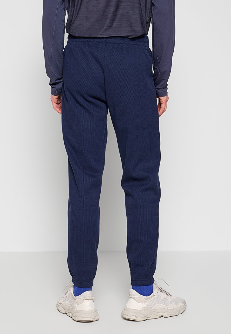 Marineblauwe sportbroek met ribbeltextuur en elastische tailleband, gecombineerd met lichtgekleurde sneakers en blauwe sokken.