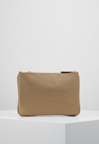 Pochette di tessuto beige con texture e chiusura a zip, caratterizzata da un accento in pelle marrone sul tira-zip. Forma rettangolare con angoli arrotondati.