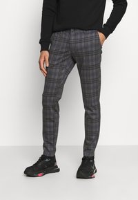 Pantalones de cuadros grises ajustados, con un tejido texturizado, que presentan líneas azules y negras. Combinados con zapatillas deportivas negras.