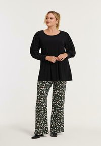 Zwarte langemouwen top met een ronde halslijn en pofmouwen, gecombineerd met bloemenpatroon broeken met een zwarte achtergrond en kleurrijke bloemen.