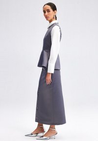 Pelēks peplum tops, kas uzlikts virs garas svārku, apvienots ar sudraba norādītā pirksta zolītēm. Iespējams, ir strukturēts dizains un gluda tekstūra.