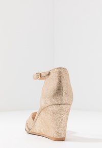 Scarpa con tacco a cuneo in oro metallico con finitura testurizzata, dotata di una sottile fascetta alla caviglia e design con punta aperta.