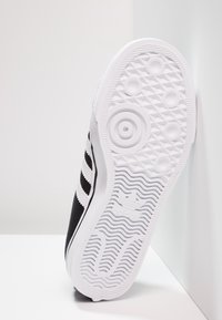 Black sneaker with a textured upper, featuring three white stripes and a white rubber sole with a patterned tread design and branding.