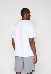 Λευκό βαμβακερό T-shirt με κοντά μανίκια, σε άνετη γραμμή. Συνδυάζεται με ανοιχτό γκρι αθλητικό σορτς, που δείχνει τις ραφές στη γαρνιτούρα.