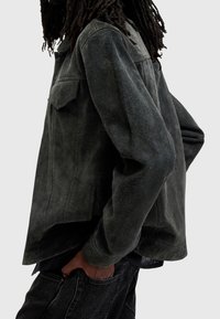 Mörkgrön mockajacka med en avslappnad passform, med spetsig krage, två bröstfickor och sidoklyftor, åtföljd av mörka denimjeans.