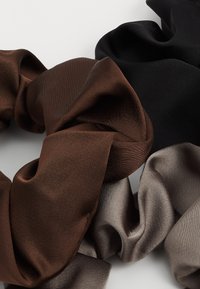 Set of three hair scrunchies in brown, black, and light gray satin, showcasing smooth textures and soft, voluminous designs.