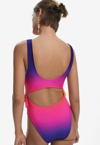 Maillot de bain une pièce avec un dégradé de rose à violet, design à dos ouvert, larges bretelles et accents orange sur les bords.