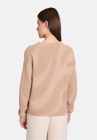 Beige gestrickter Pullover mit strukturiertem Finish und einem Wellenmuster. Lockere Passform mit rundem Halsausschnitt und gerippten Bündchen.