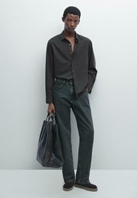 Zwarte, lange mouw button-up shirt in combinatie met donkergrijze rechte jeans. Een donkere leren schoudertas en bruine instapschoenen maken de outfit compleet.
