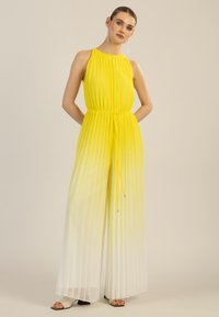 Jumpsuit amarillo con pliegues, cuello halter, cintura ceñida y degradado hacia el blanco. Presenta un cordón ajustable con acentos plateados.