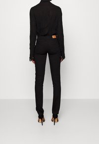 Zwarte, gestructureerde blouse met lange mouwen en een gekreukt patroon, gecombineerd met slim-fit zwarte broek en hoge hakken, gezien vanaf de achterkant.