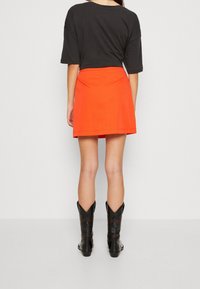 Svart kort t-shirt, ljusorange mini kjol, och svarta cowboyboots med intrikata texturer och design detaljer.