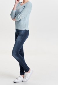Lichtblauwe gebreide trui met 3/4 mouwen, gecombineerd met donkerblauwe skinny jeans en witte sneakers. Glad textuur en casual ontwerp.