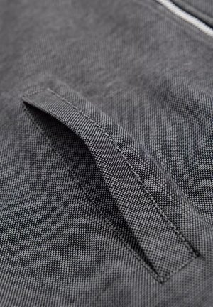 Tejido gris con una superficie texturizada que presenta una apertura de bolsillo cosida. El diseño es elegante, con un detalle sutil y un acabado limpio.